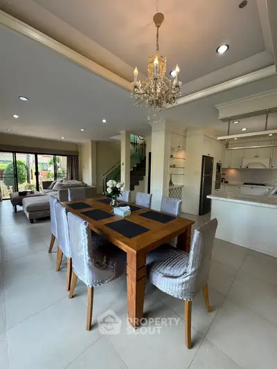 Elegant open-plan living and dining area with chandelier and modern kitchen.