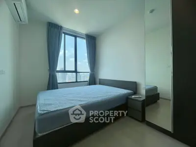 Modern bedroom with large window and city view, featuring sleek furniture and natural light.