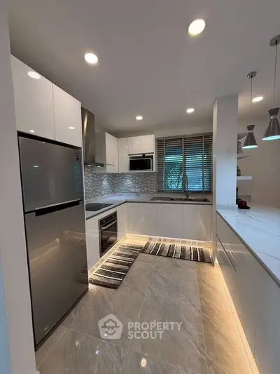 Modern kitchen with sleek white cabinets, stainless steel appliances, and elegant lighting.
