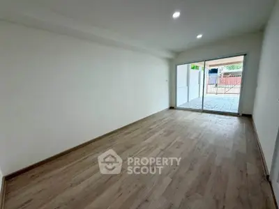 Spacious empty room with wooden flooring and large sliding glass doors leading to a patio.