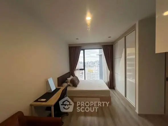 Modern bedroom with city view, featuring a cozy bed, study desk, and large window with curtains.