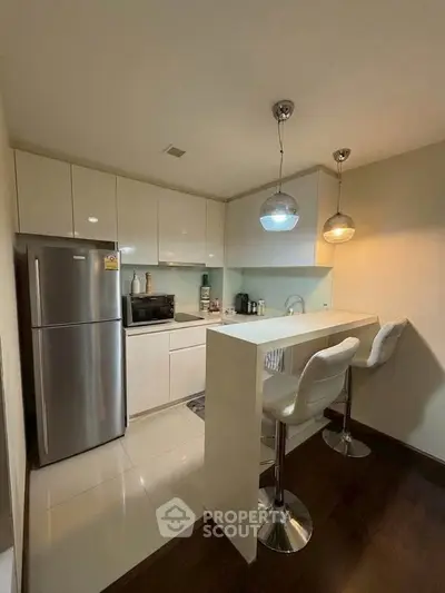 Modern kitchen with sleek white cabinets and breakfast bar, featuring stainless steel appliances and stylish lighting.