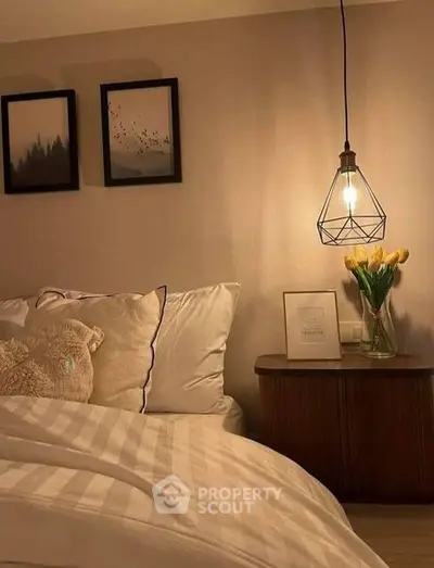 Cozy bedroom corner with stylish bedding, elegant side table, fresh flowers, and unique pendant light, perfect for a restful retreat.