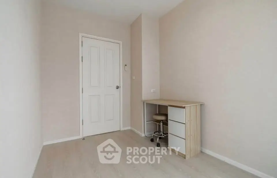 Minimalist study room with desk and chair, featuring light wood flooring and neutral walls.