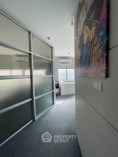 Modern office space with frosted glass partitions and vibrant wall art, featuring ample natural light.