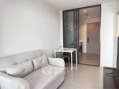 Modern living room with sleek design and glass partition, featuring a cozy sofa and compact dining area.