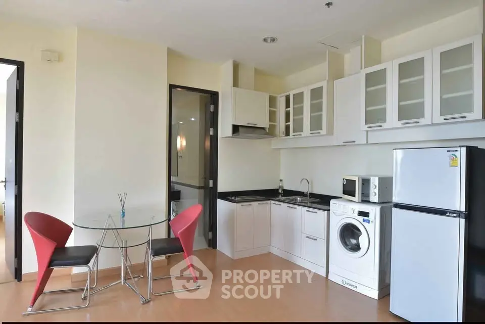 Modern kitchen with dining area, featuring white cabinets, washing machine, and fridge.