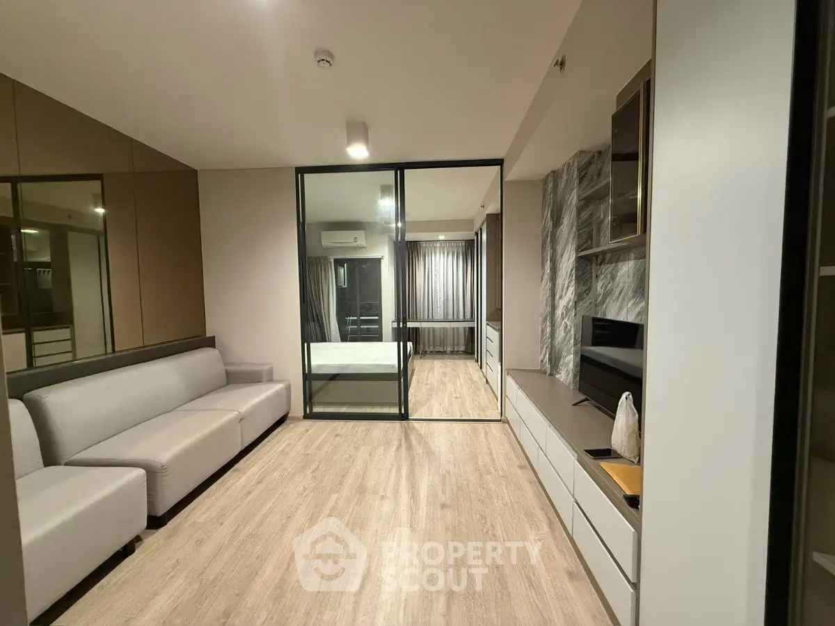 Modern living room with sleek design and glass partition leading to bedroom