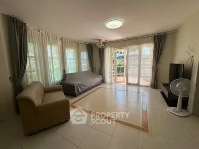 Spacious living room with large windows and balcony access, featuring modern furniture and ample natural light.