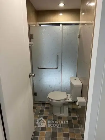 Compact bathroom with modern shower and tiled floor in cozy apartment.