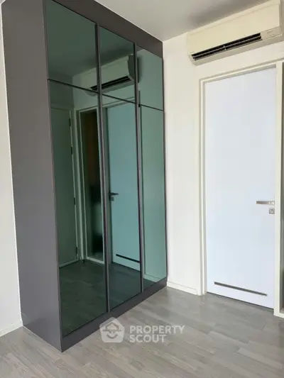 Modern bedroom with sleek mirrored wardrobe and air conditioning unit.