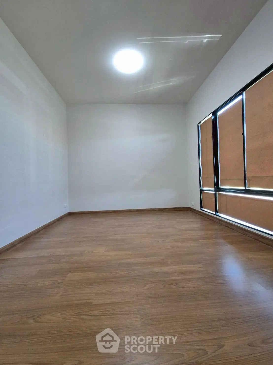 Spacious empty room with wooden flooring and large window, perfect for customization.