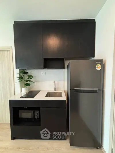Modern kitchen with sleek black cabinets and stainless steel fridge in a compact layout.