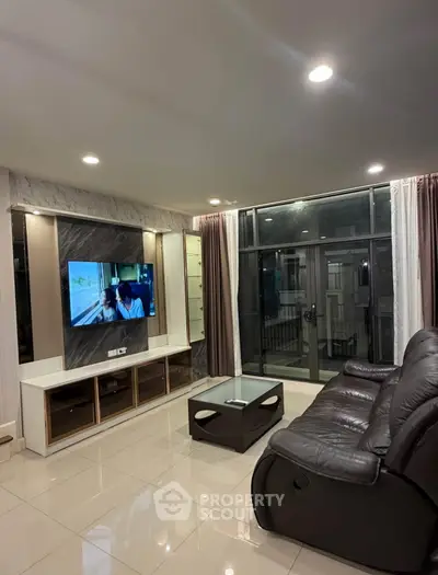 Spacious modern living room with leather sofa and large TV, featuring elegant lighting and floor-to-ceiling windows.