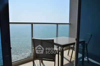 Stunning ocean view from modern balcony with glass railing and outdoor seating.