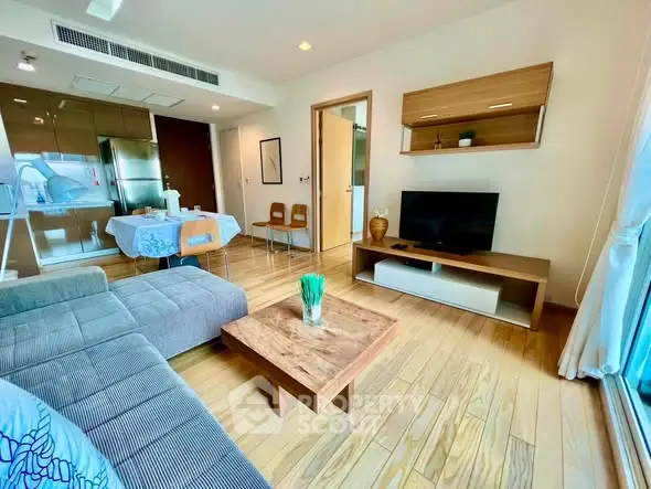 Modern living room with wooden flooring, cozy sofa, and sleek kitchen area in open layout apartment.