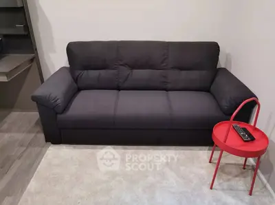 Modern living room with sleek black sofa and vibrant red side table.