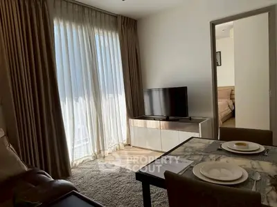 Cozy living room with TV and dining area, adjacent to a bedroom, featuring elegant curtains and soft lighting.