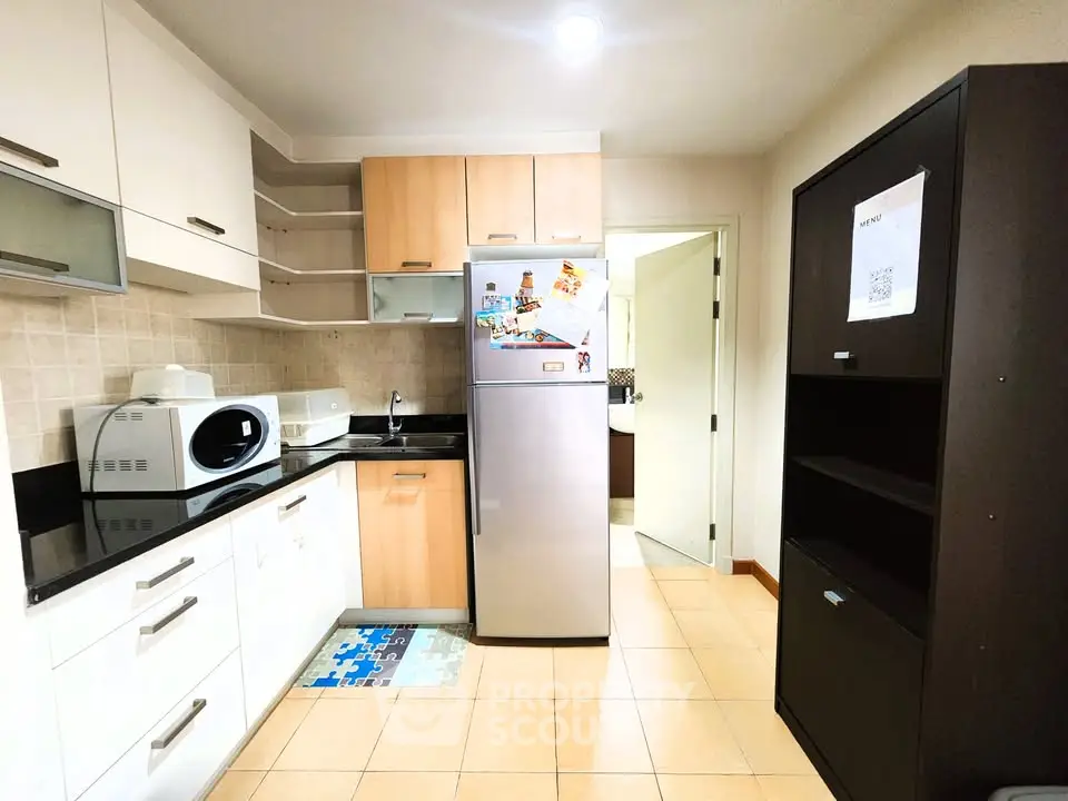 Modern kitchen with sleek cabinets and stainless steel fridge in cozy apartment.