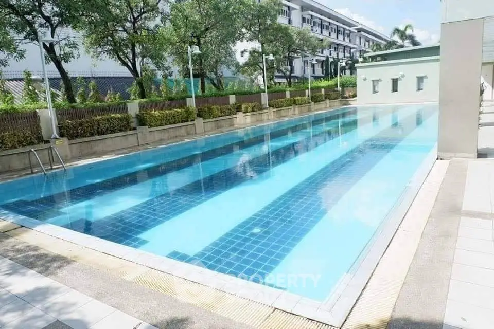 Luxurious outdoor swimming pool in a modern residential complex with lush greenery.