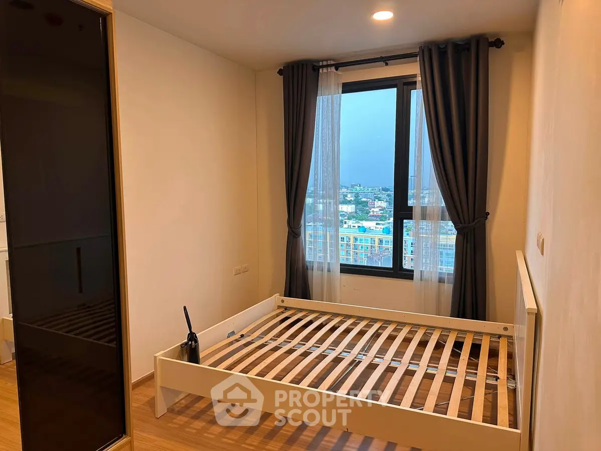 Spacious bedroom with large window offering city views, featuring a modern bed frame and sleek wooden flooring.