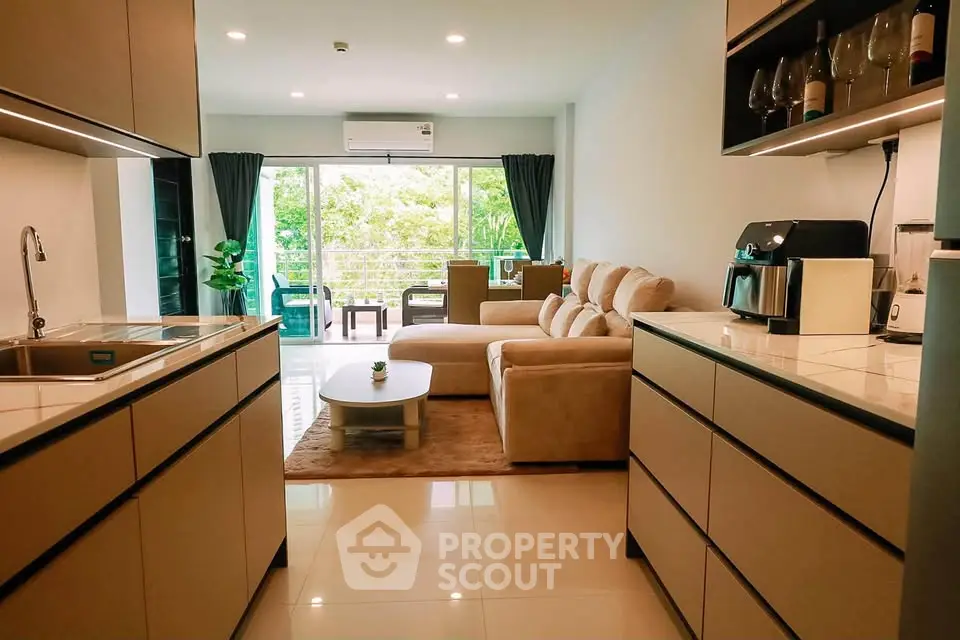 Modern open-layout kitchen and living room with cozy sofa and large windows offering a green view.