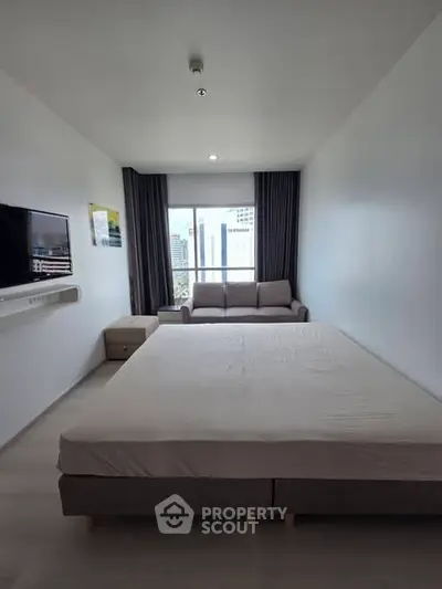 Spacious modern bedroom with city view, featuring a large bed and cozy seating area.