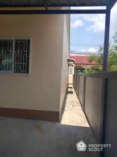 Narrow side pathway alongside a modern house with a secure window and clear sky view.