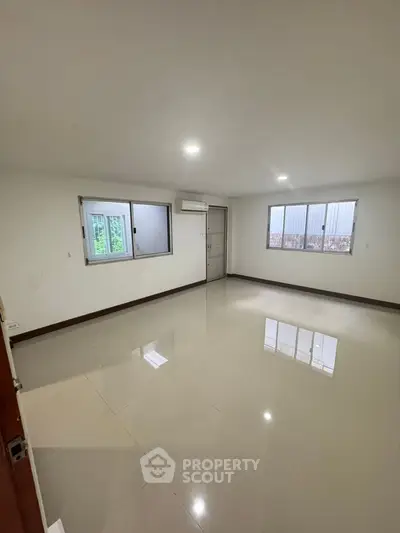 Spacious empty room with glossy tiled flooring and large windows, perfect for customization.