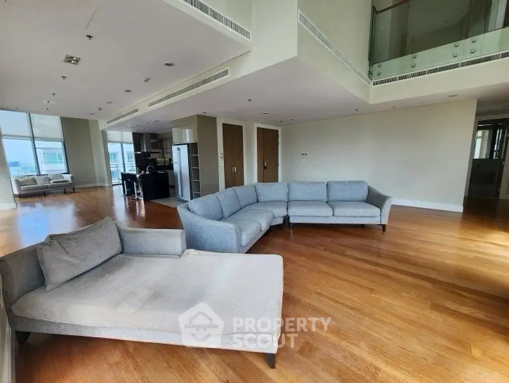 Spacious modern living room with elegant furniture and open layout, featuring large windows and wooden flooring.