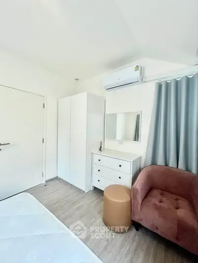 Cozy bedroom with modern furniture and air conditioning, featuring a plush chair and stylish decor.