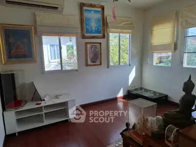 Bright living room with wooden floors and religious decor, featuring large windows and air conditioning.