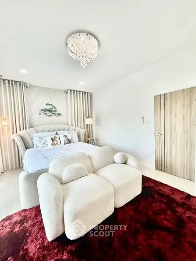 Luxurious bedroom with plush seating and elegant chandelier, featuring modern decor and cozy ambiance.