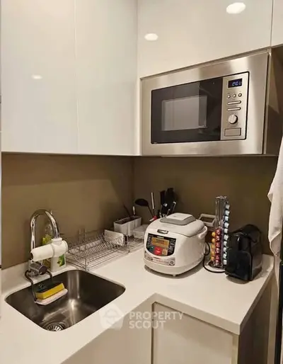 Compact modern kitchen with microwave and rice cooker, ideal for efficient cooking.