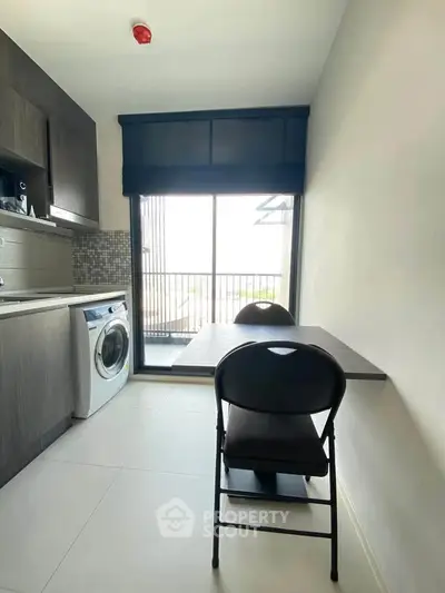 Modern kitchen with washing machine and dining area, featuring sleek cabinetry and natural light.