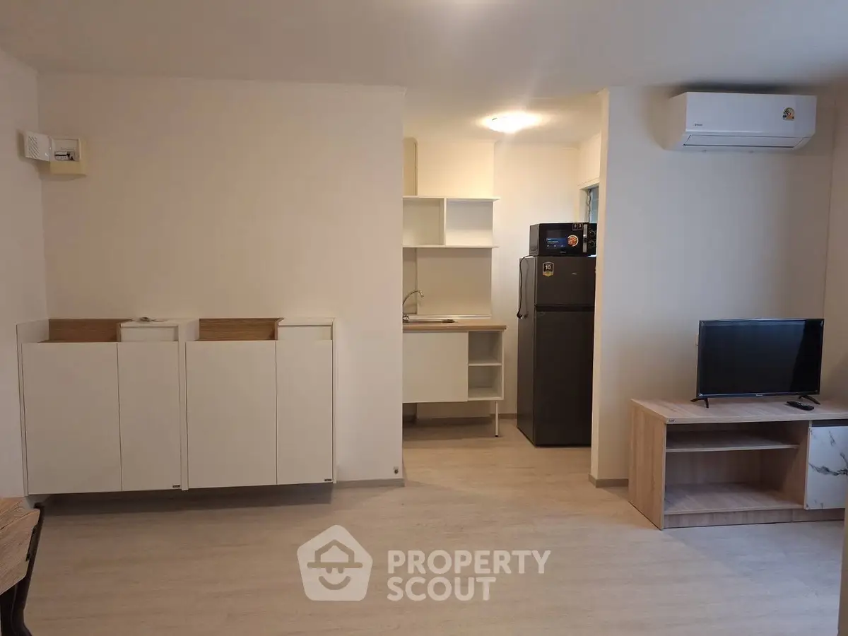 Modern apartment interior with compact kitchen and living area, featuring sleek cabinetry and air conditioning.