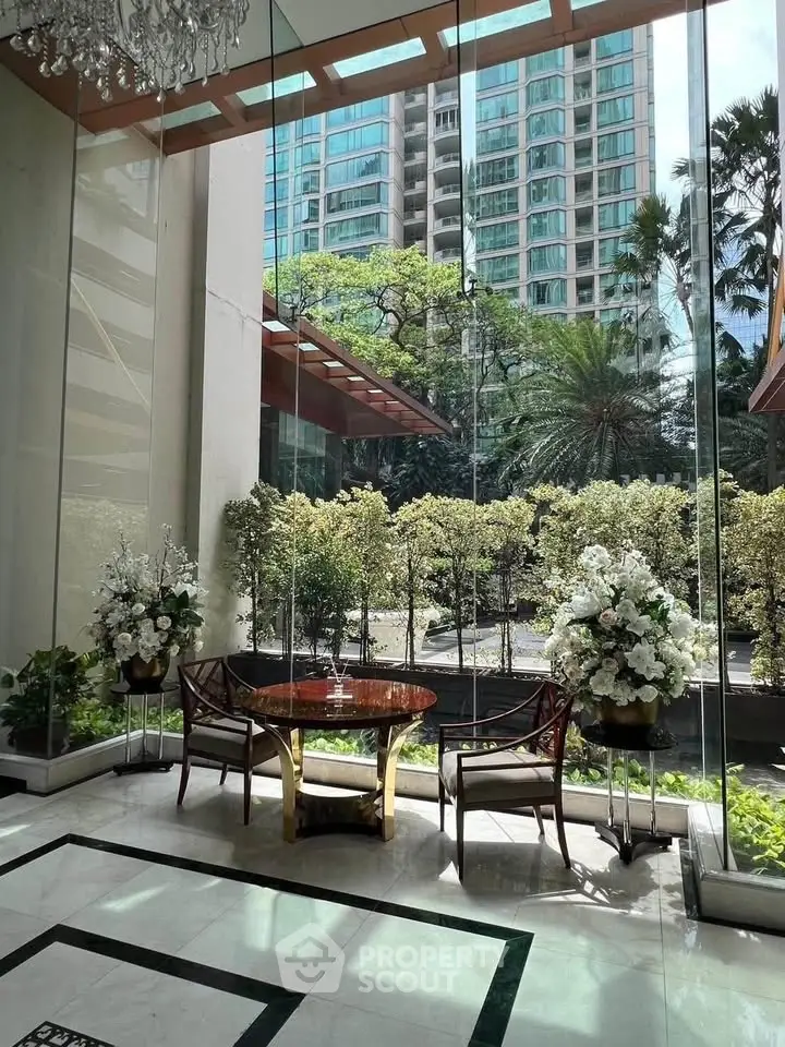Luxurious building entrance with elegant seating and lush greenery view.