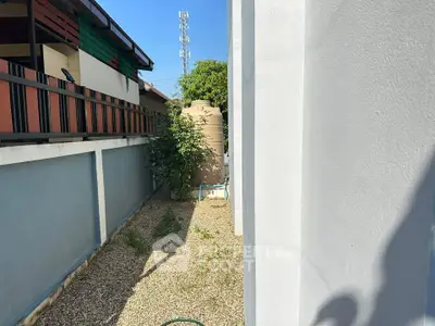 Narrow side yard with gravel and a water tank, adjacent to a modern building exterior.