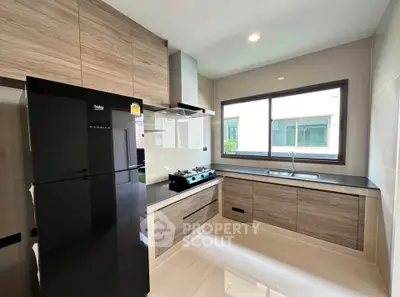 Modern kitchen with sleek cabinetry and large window, featuring a black refrigerator and gas stove.