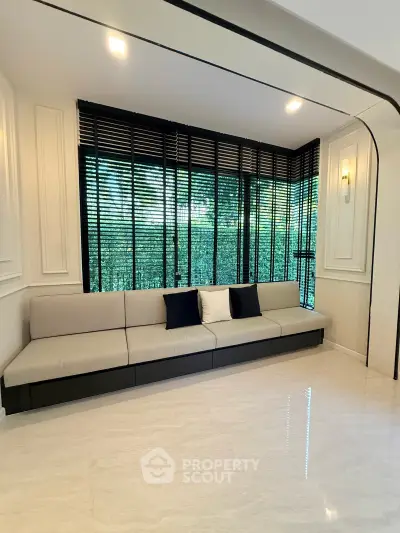 Elegant living room with modern sofa and large windows with blinds, offering a serene garden view.