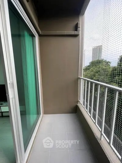 Modern apartment balcony with sliding glass doors and safety netting, offering a serene view of greenery.