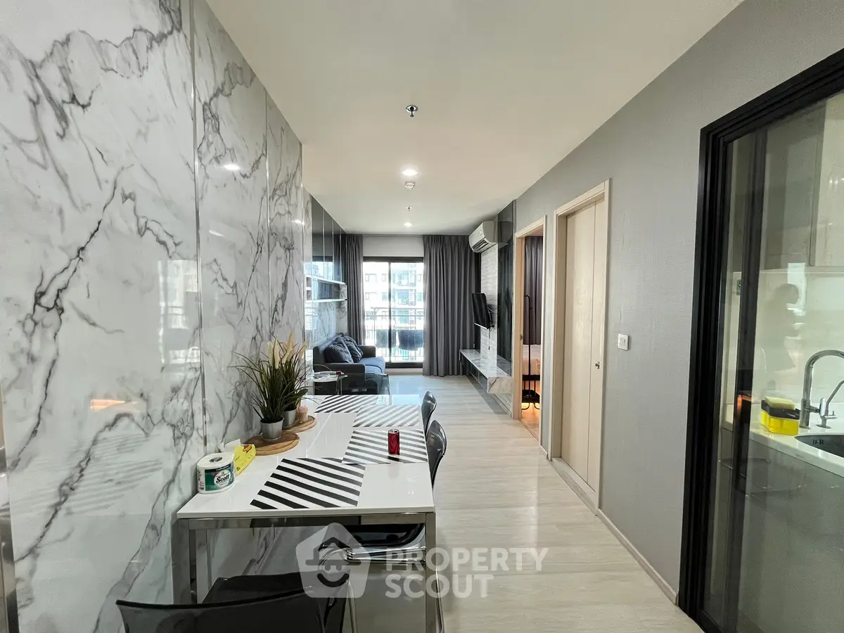 Modern apartment interior with marble wall, open living area, and sleek kitchen design.