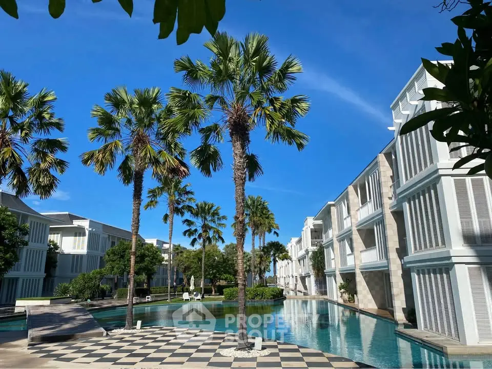 Luxurious resort-style pool area with palm trees and modern architecture under a clear blue sky.