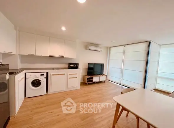 Modern open-plan living room with kitchen, featuring wooden flooring and natural light.