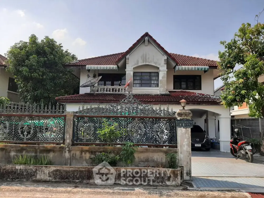 Charming two-story house with red-tiled roof and ornate iron fence