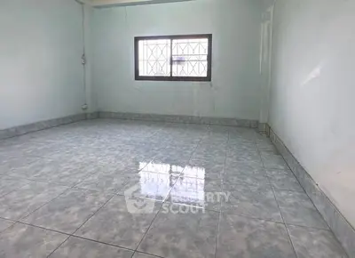 Spacious empty room with tiled flooring and barred window, ideal for customization.