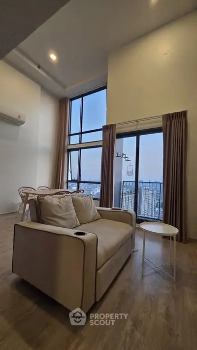 Spacious living room with high ceilings and stunning city view, featuring modern furniture and large windows.