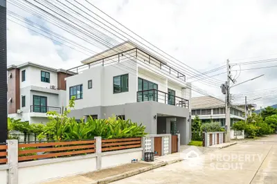 Modern two-story house with rooftop terrace and lush garden in suburban neighborhood.