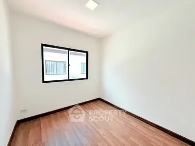 Spacious empty room with wooden flooring and large window, perfect for customization.