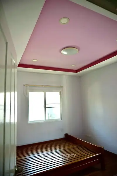Cozy bedroom with unique pink ceiling and wooden bed frame, perfect for a stylish retreat.